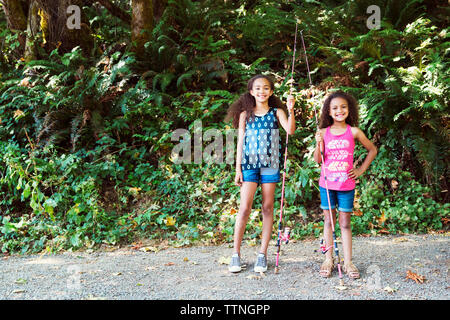 Portrait of sisters with fishing rods standing footpath against trees Stock Photo