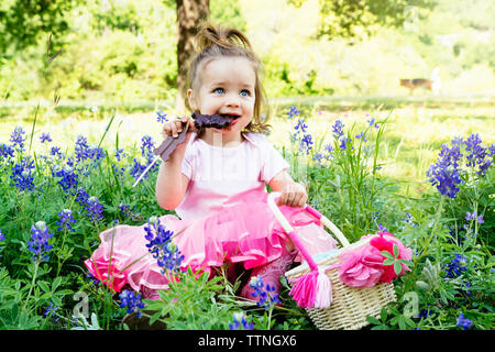 Girl eating chocolate easter bunny while sitting on field amidst flower Stock Photo