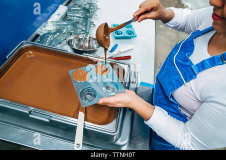 High angle midsection of baker pouring chocolate in mold at factory Stock Photo