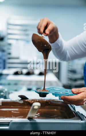 Cropped hands of baker pouring chocolate in mold at factory Stock Photo