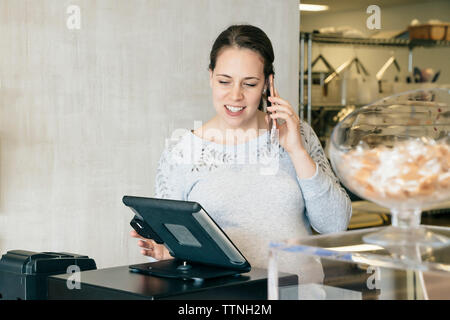 Woman talking on mobile phone while using tablet computer at store Stock Photo