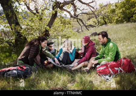 Happy friends looking at map while sitting on grassy field Stock Photo