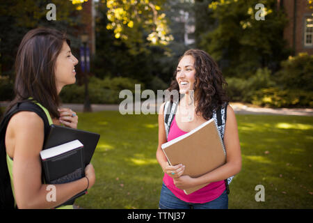Happy female friends discussing while standing at lawn Stock Photo