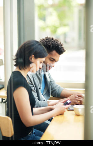 Multi-ethnic couple using smart phone in cafe Stock Photo