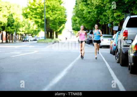 Portrait of female athlete friends running on road against trees in city Stock Photo