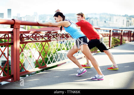 Athlete friends exercising on footbridge against sky in city Stock Photo
