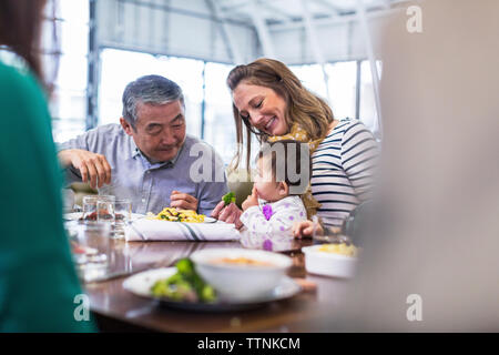 Family looking at cute baby boy eating food in restaurant Stock Photo