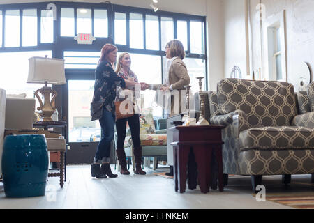 Woman looking at owner doing handshake with friend in furniture store Stock Photo