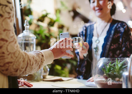 Midsection of customer holding mobile phone while owner scanning QR code in plant shop Stock Photo