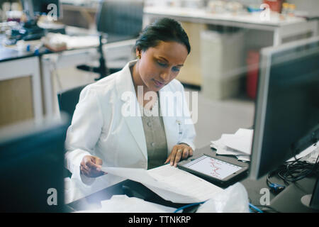 Female doctor examining reports at desk in hospital seen through glass Stock Photo