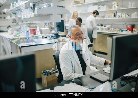 Male doctor using desktop computer while coworkers working in background at hospital Stock Photo