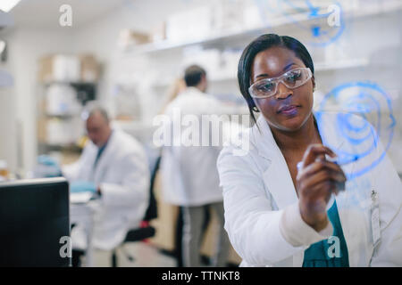 Female doctor writing on glass window with coworkers in background at medical room Stock Photo