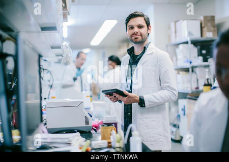 Portrait of male doctor with tablet computer and coworkers working in medical room Stock Photo