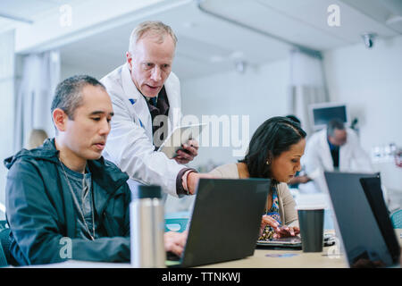 Male doctor discussing with coworkers over laptop computer in medical room Stock Photo