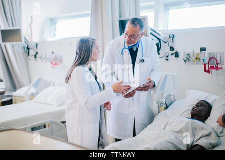Male doctor discussing with female coworker over tablet computer in hospital ward Stock Photo