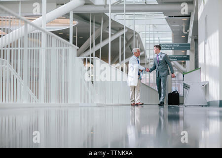 Male doctors shaking hands while walking in hospital corridor Stock Photo