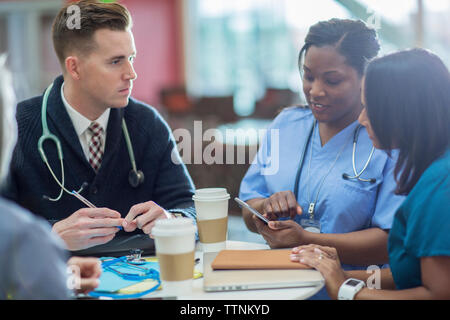 Male doctor looking at female doctors discussing over tablet computer in meeting at medical room Stock Photo