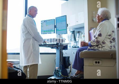 Male doctor talking to female patient while using computer in hospital ward Stock Photo