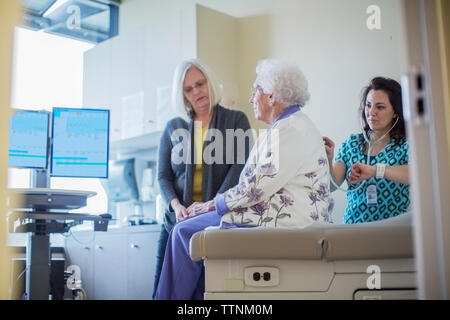 Daughter looking at female doctor listening mother's breathing in hospital ward Stock Photo