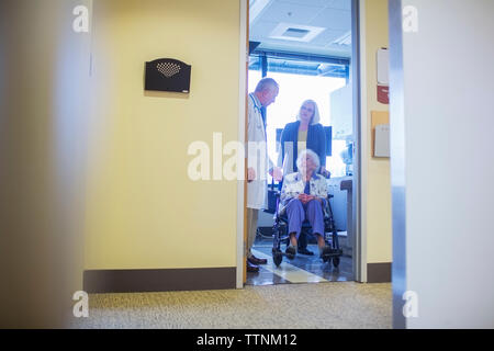 Daughter assisting mother sitting on wheelchair while talking to doctor in hospital ward Stock Photo