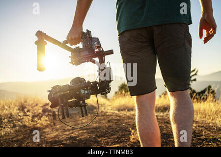 Midsection of man holding shoulder stand camera while standing on mountain during sunny day Stock Photo