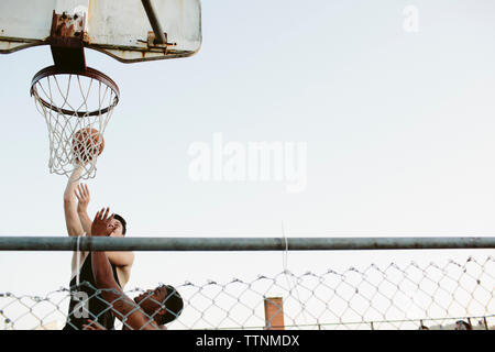 Low angle view of friends playing basketball against clear sky Stock Photo