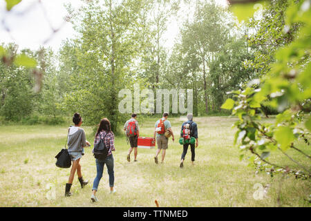 Full length of friends with backpack walking on field in forest Stock Photo
