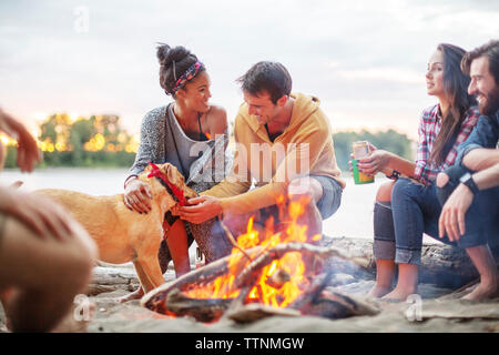 Happy friends with dog by campfire against river Stock Photo