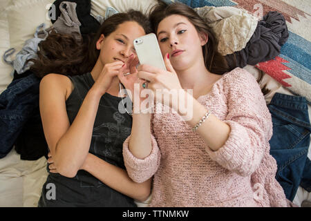 Overhead view of female friends using smart phone while lying on bed at home Stock Photo