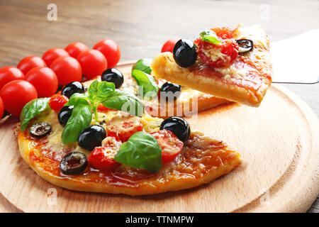 Sliced tasty pizza and fresh cherry tomatoes on wooden plate Stock Photo