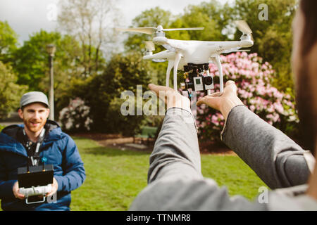 Man operating quadcopter while friend holding it in park Stock Photo