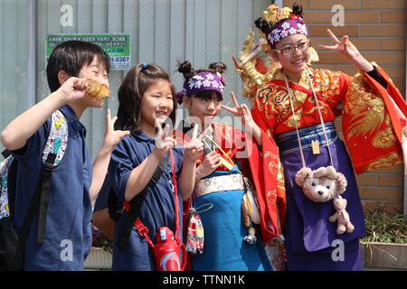 Four Japanese children two in modern dress and two in kimonos posing with the pīsu sain or peace gesture of two fingers Stock Photo