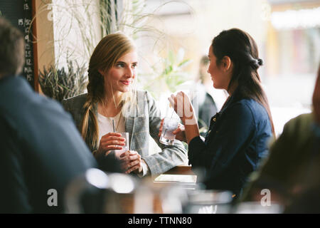 Female friends talking while having drinks by window in restaurant Stock Photo