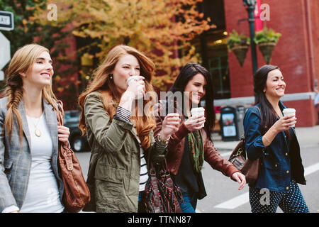Happy female friends having coffee while walking on city street Stock Photo