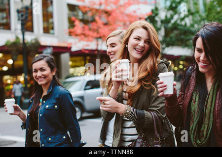 Cheerful female friends having coffee while walking on city street Stock Photo