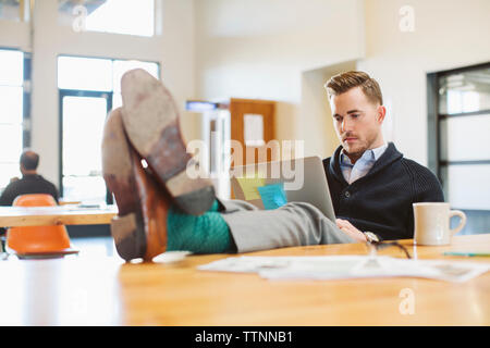 businessman using laptop computer at desk in office while colleague working in background Stock Photo