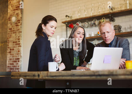 Colleagues looking at laptop computer while discussing in office Stock Photo