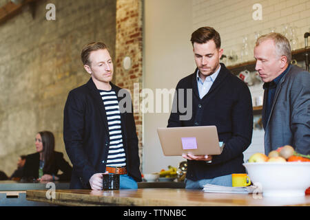 businessman using laptop computer while standing with male colleagues in office Stock Photo