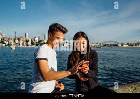 Happy young couple using smart phone while exercising on promenade against Sydney Harbour Bridge Stock Photo