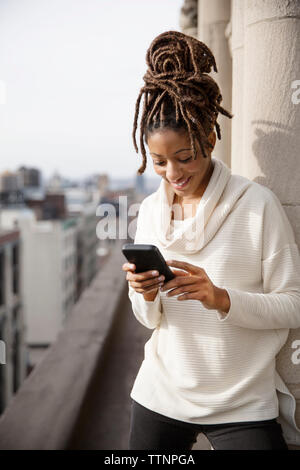 Smiling woman using smart phone while standing on balcony Stock Photo