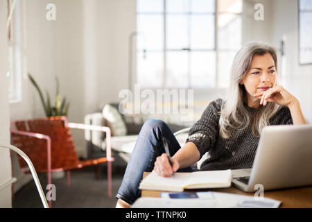 Mature woman writing in diary while working at home Stock Photo