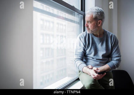 Thoughtful mature man looking through window at home Stock Photo