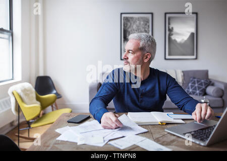 Thoughtful man looking away while calculating home finances at table Stock Photo