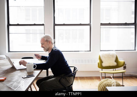 Side view of man using laptop computer while sitting at home Stock Photo