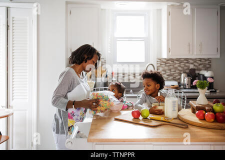 Mother serving breakfast cereals to children at kitchen island Stock Photo