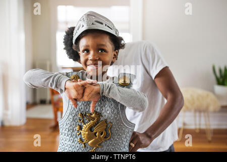 Father assisting cheerful boy in getting dressed as armor at home Stock Photo