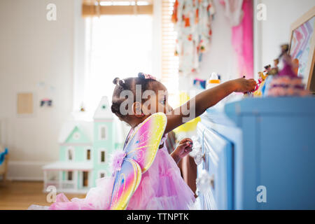 Side view of girl dressed in fairy costume playing with toys at home Stock Photo