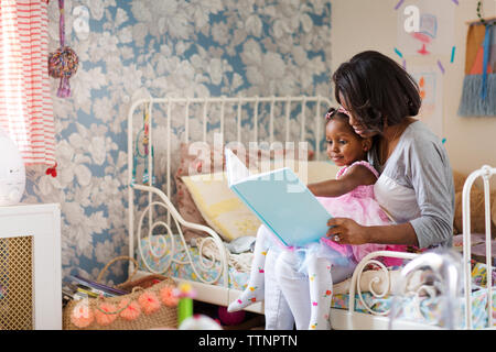 Girl looking at picture book with mother in bedroom Stock Photo