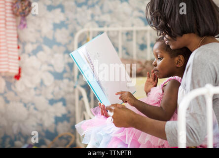 Girl pointing at picture book while sitting with mother in bedroom Stock Photo