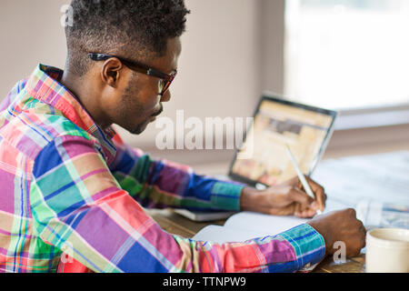 Side view of man writing in book while working at home Stock Photo